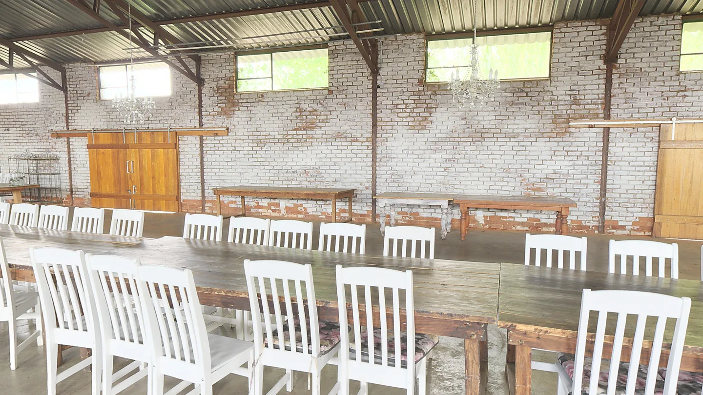 De feestschuur met lange tafels, witte stoelen en kroonluchters.