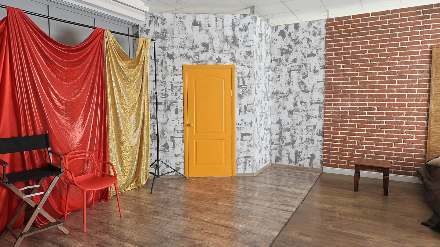Een set in de fotostudio: rode en gouden doeken, een gele deur en een bakstenen muur.