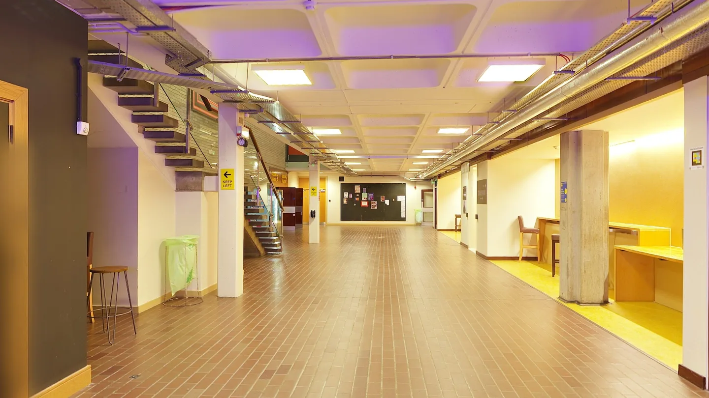 De hal van de school, met een trap links en werkplekken rechts.